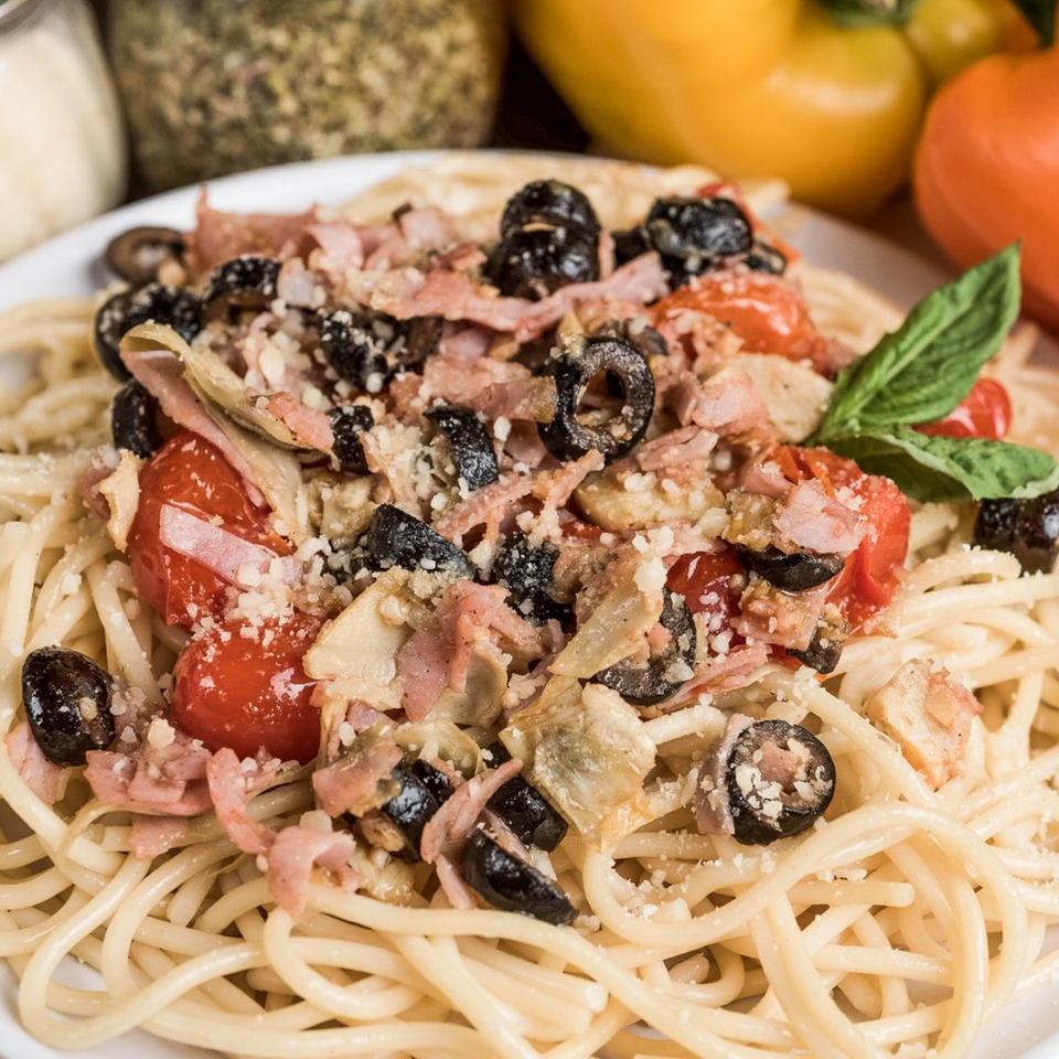 Spaghetti with tomatoes, olives, ham, artichokes, and Parmesan cheese, garnished with basil.