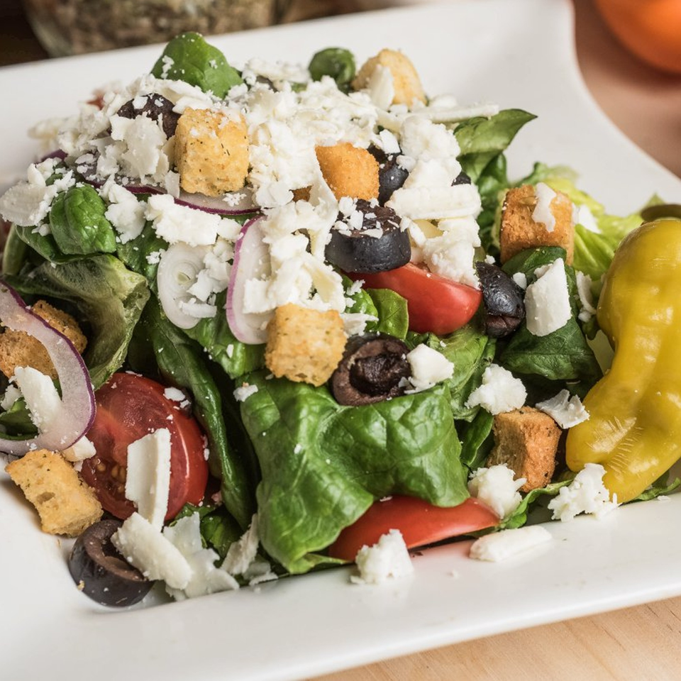 A fresh Roma's Pizza salad with lettuce, tomatoes, olives, onions, croutons, and feta cheese.