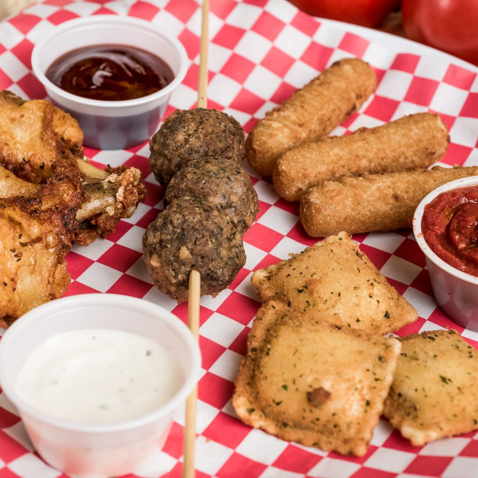 A platter of fried appetizers including wings, meatballs, mozzarella sticks, and toasted ravioli with dipping sauces.